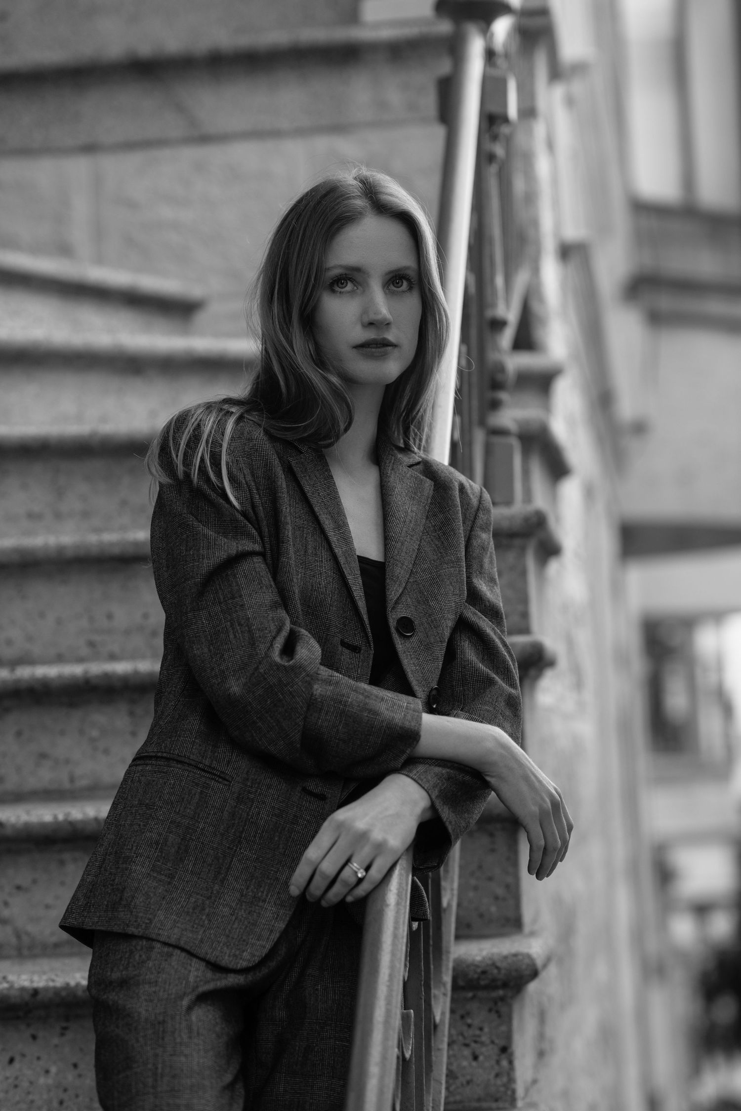 Black and white fashion portrait of someone in an oversized blazer posing on concrete steps.
