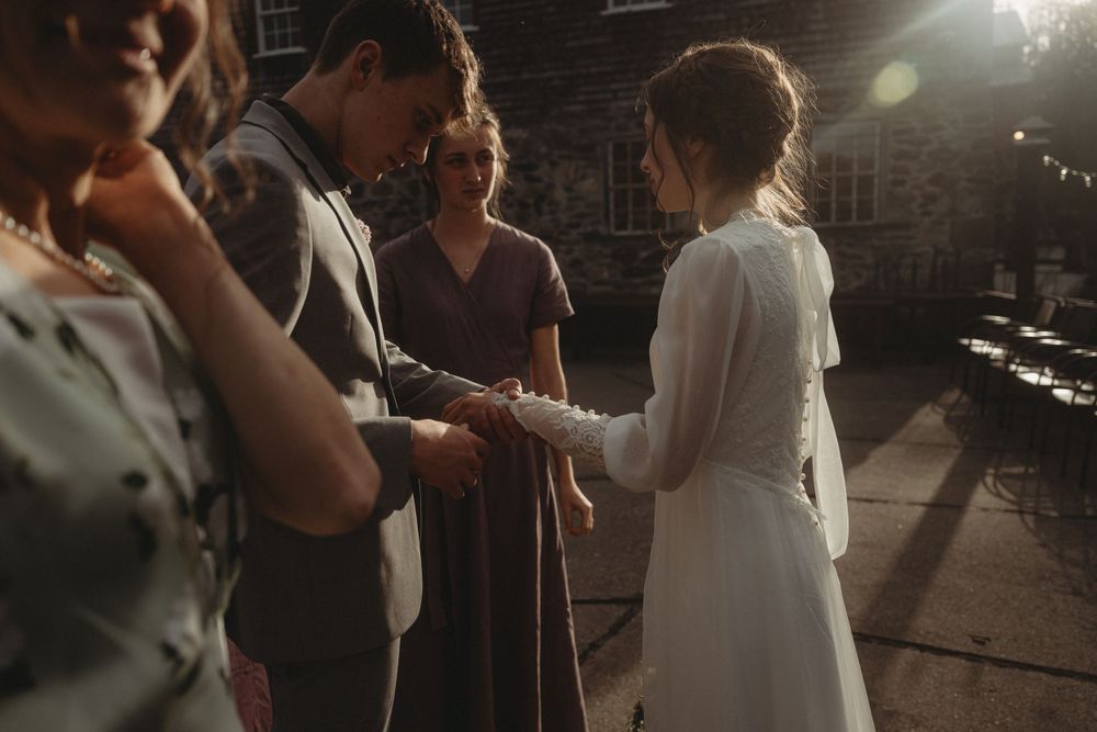 Wedding ceremony moment captured in dramatic evening lighting against brick wall backdrop.