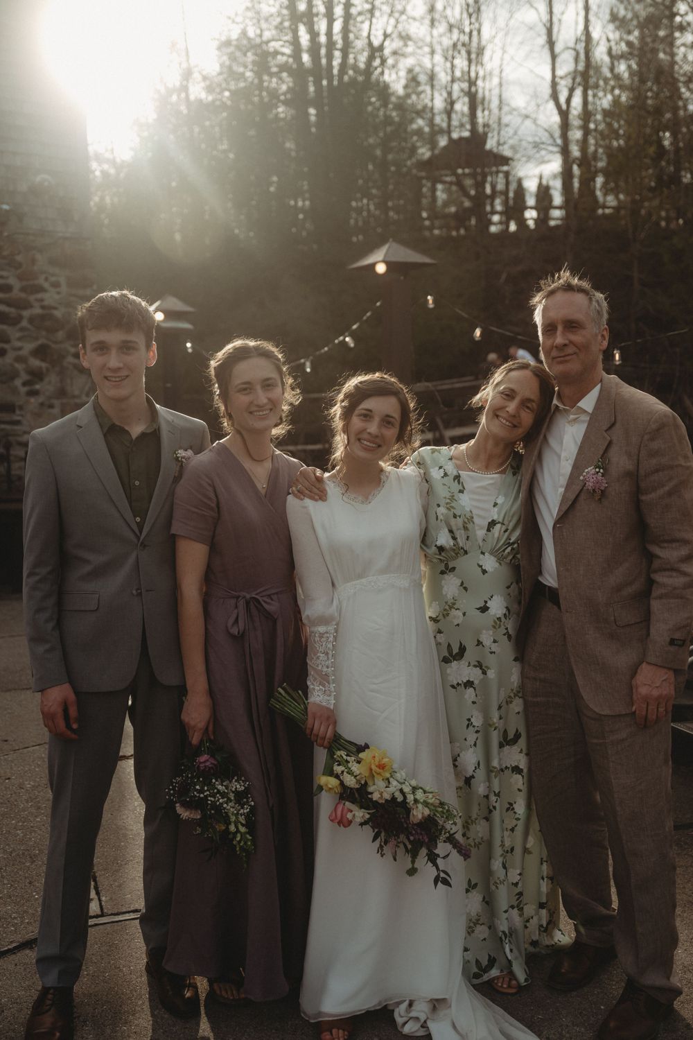Wedding party poses together at sunset with trees and gazebo in background.