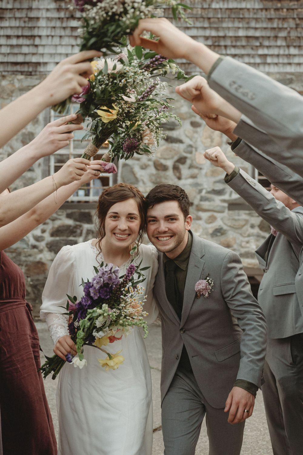Wedding celebration with guests raising floral bouquets around the happy couple.