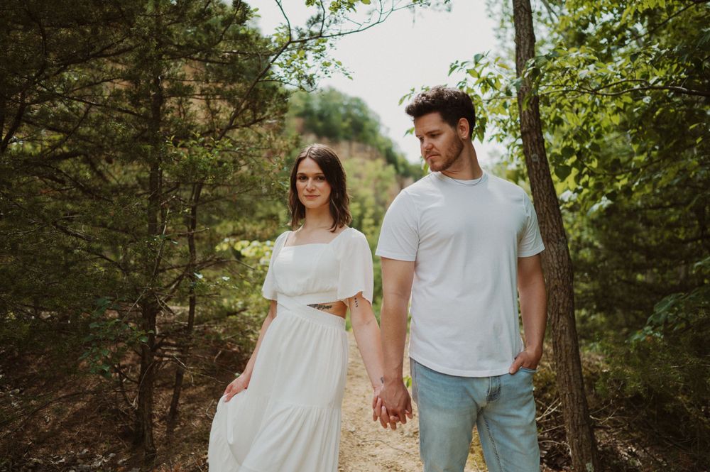 A couple in matching white outfits sharing an intimate moment in a sunlit forest setting.