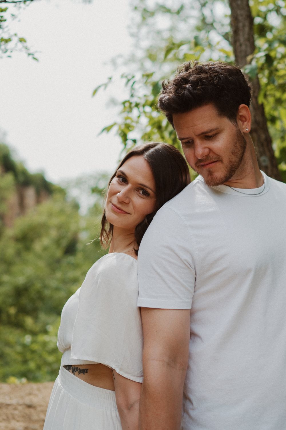 Tender moment between a couple wearing white clothes as they pose together in a forest setting.
