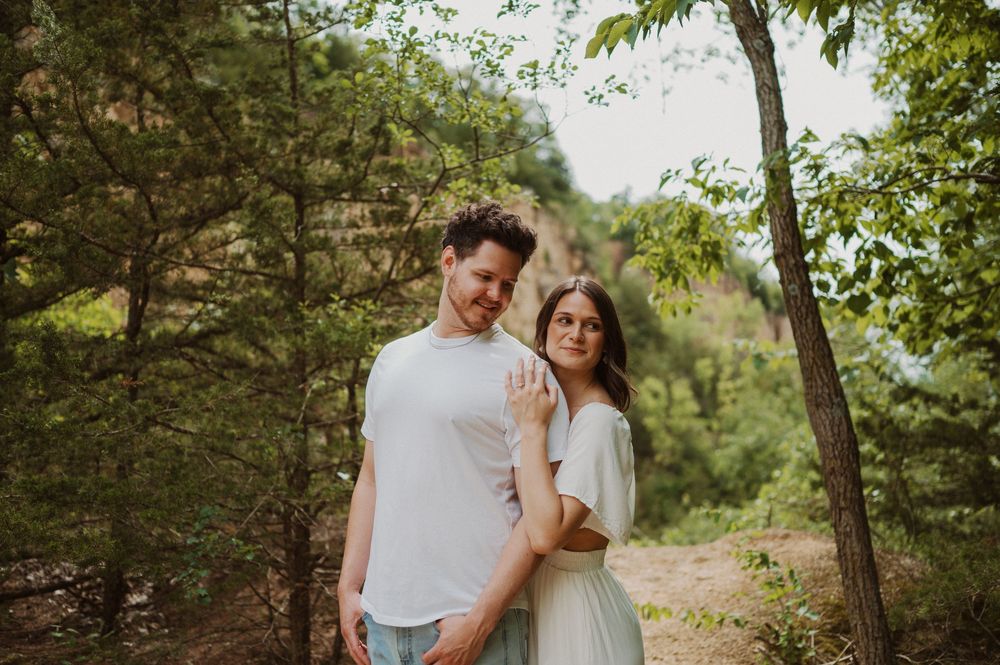 A couple shares tender moments during an engagement photo session in a lush natural setting with golden sunlight.