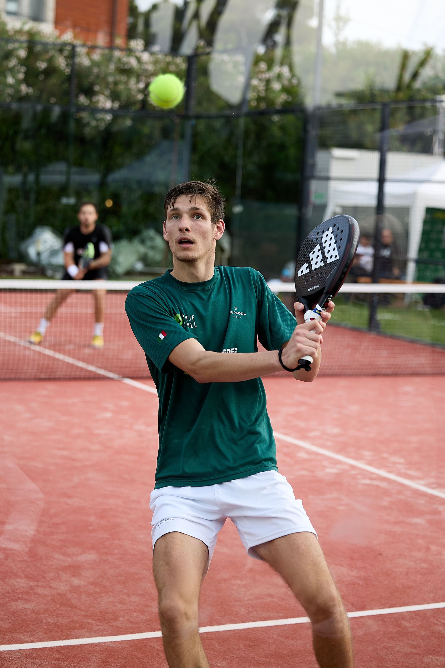 Player prepares to hit return shot during padel tennis match on outdoor court.