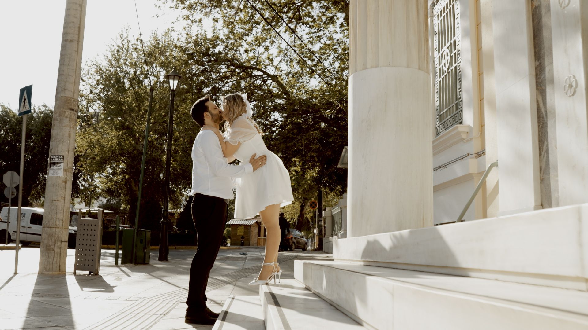 A romantic embrace on white stone steps with classical columns in the background.