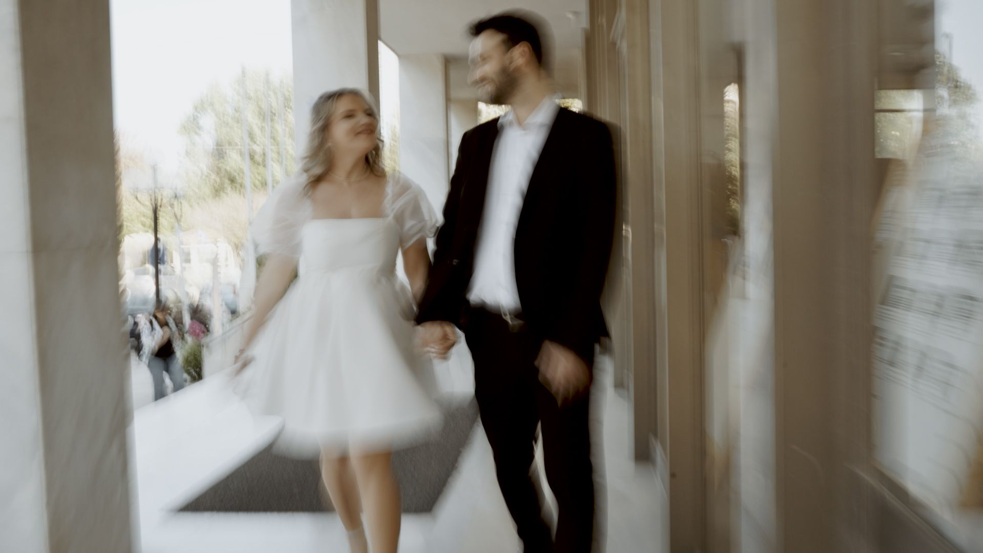 A happy couple in wedding attire dancing in a bright hallway.