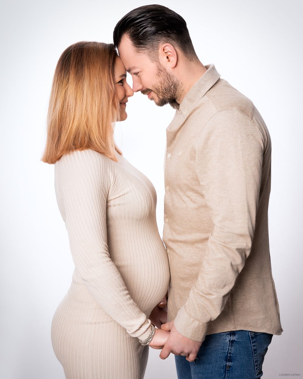 studio fotoshoot van aanstaande ouders voor witte achtergrond. ze staan tegen elkaar aan met hun voorhoofd tegen elkaar aan.