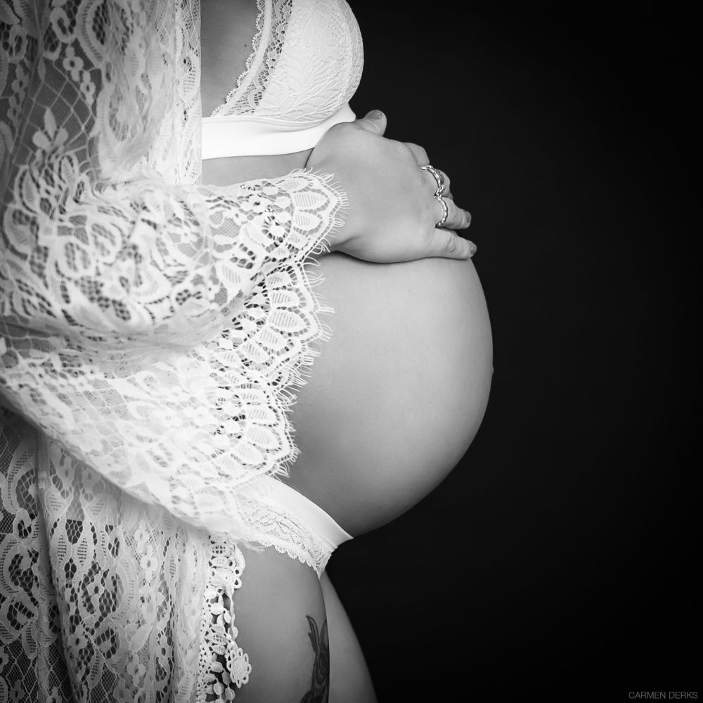 zwart wit foto van zwangere buik met kanten vestje en ondergoed, zwangere vrouw houdt haar buik vast. zwarte achtergrond in een studio.