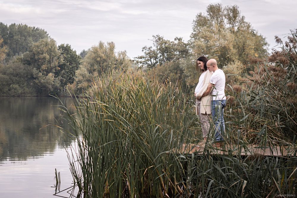 aanstaande ouders tijdens hun zwangerschapsshoot staan model bij een vijver tussen het groen. gefotografeerd in maas en waal