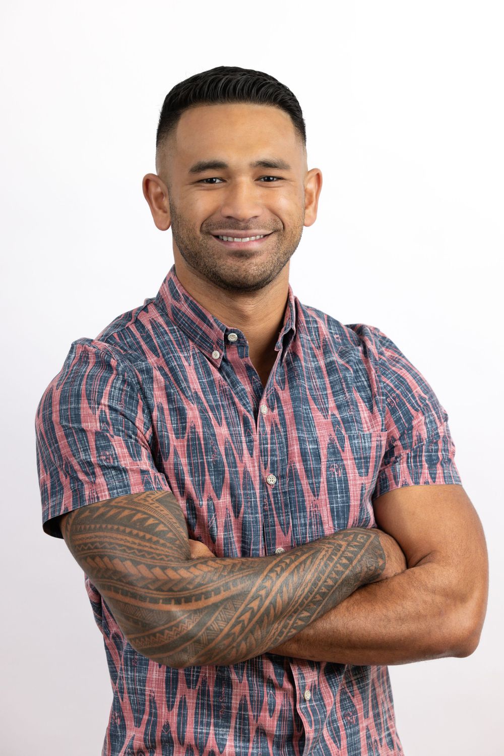 Professional portrait of man in patterned shirt showing tattoo sleeve against white background.
