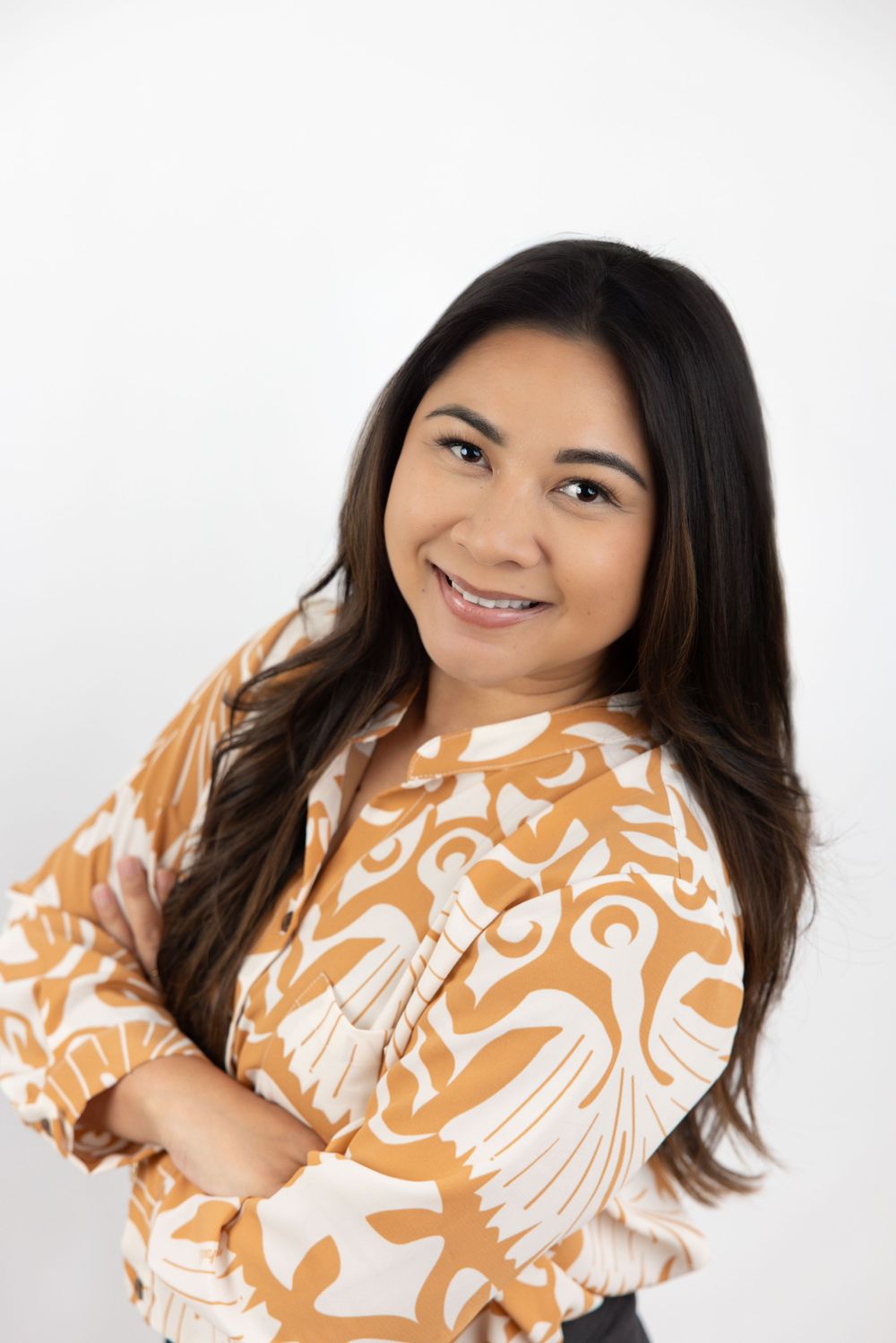 Studio portrait of woman in orange and white patterned blouse against white background.
