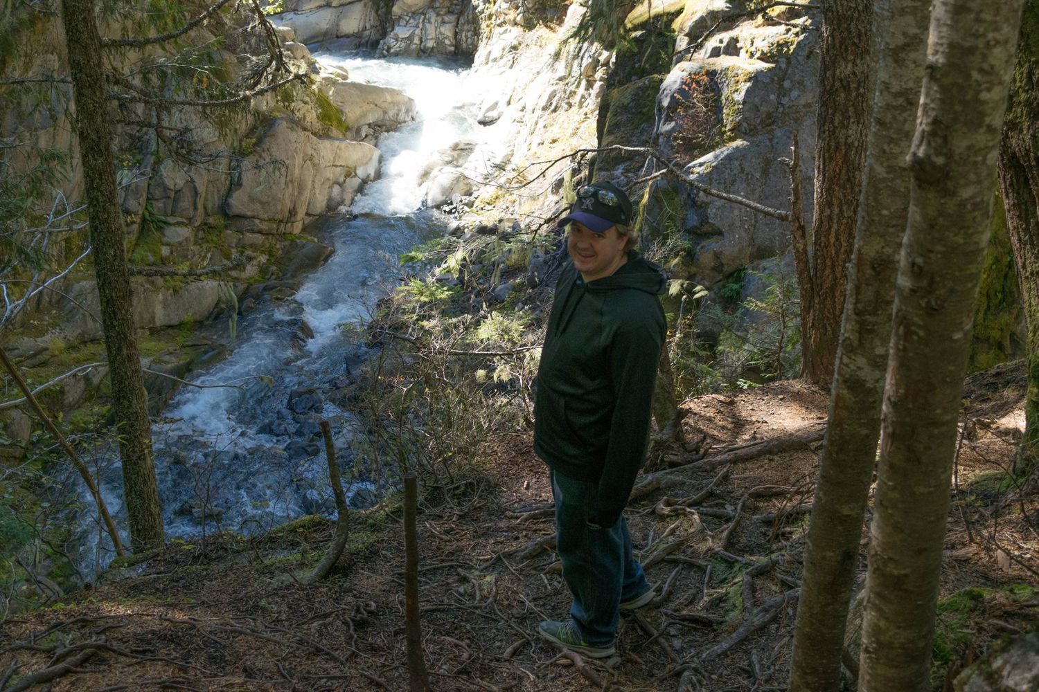 Someone views a rushing waterfall from a rocky forest trail overlook.