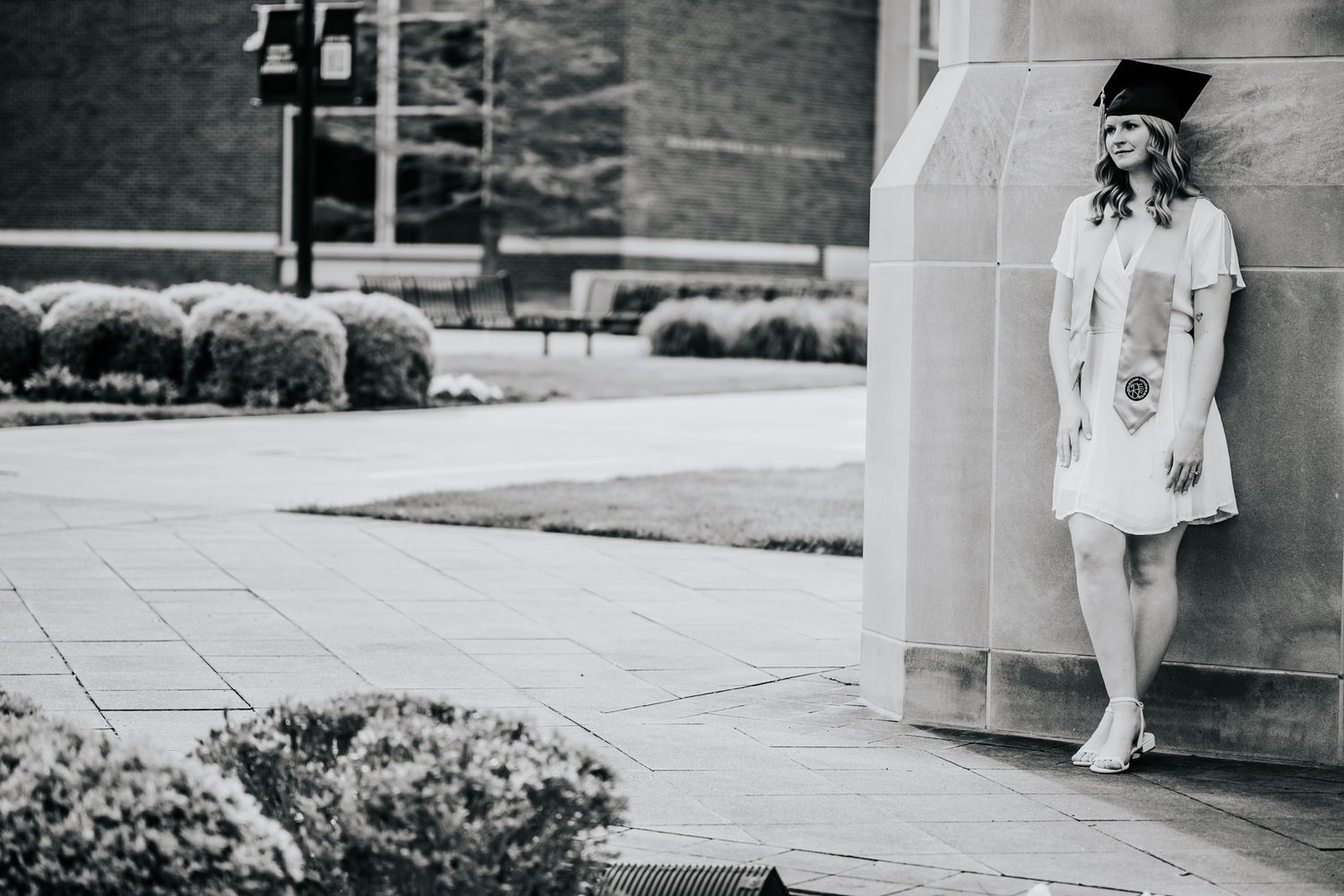 Black and white photo of person in vintage dress leaning against building column.