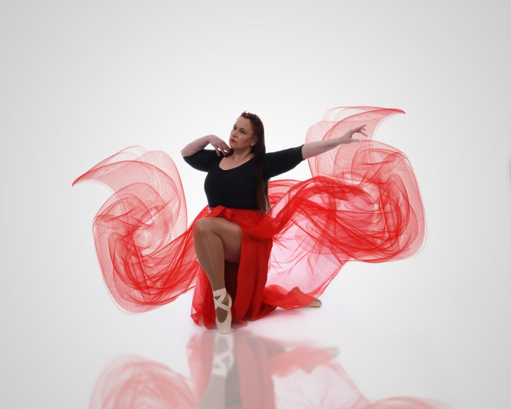 A dancer performs with flowing red fabric against a white background creating dynamic movement and energy in the composition.