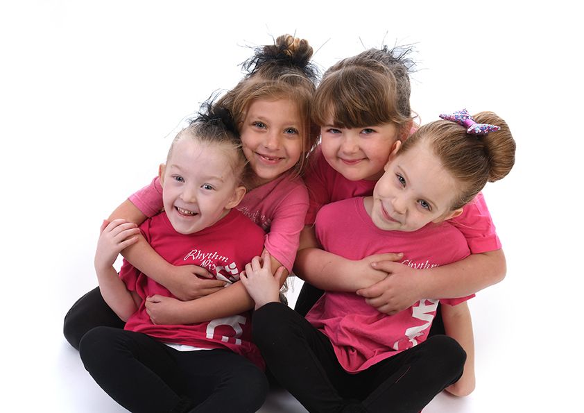Dance group in matching pink shirts huddle together for casual portrait.