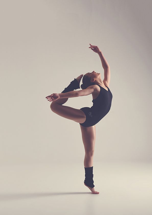 Contemporary dancer in black leotard executes dramatic pose with extended leg in studio setting.
