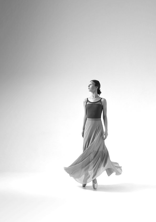 Graceful dancer in flowing skirt moves elegantly against light background in black and white photograph.
