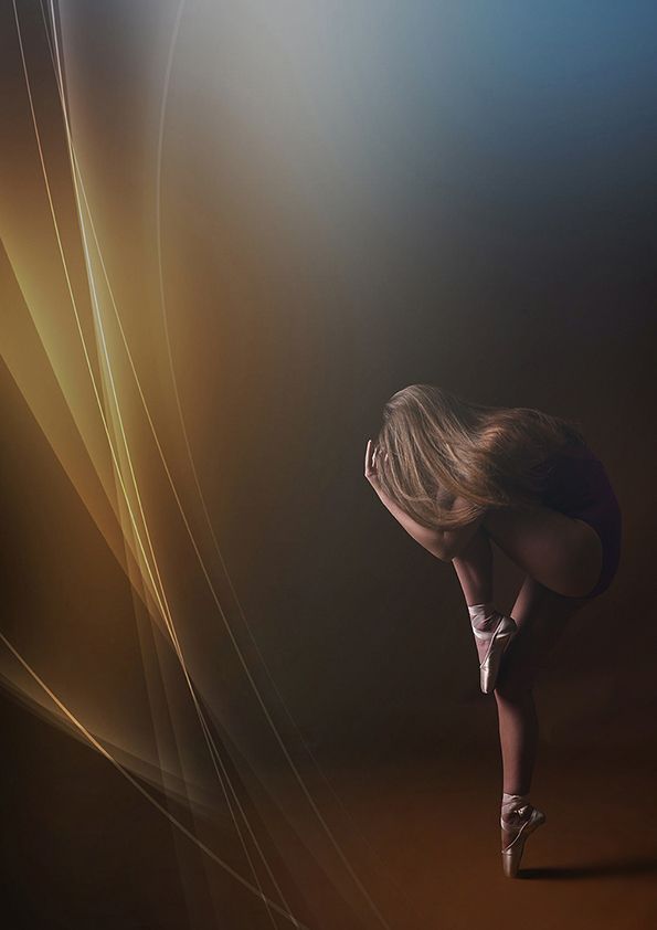 Artistic ballet pose silhouetted against warm light streams and abstract background.