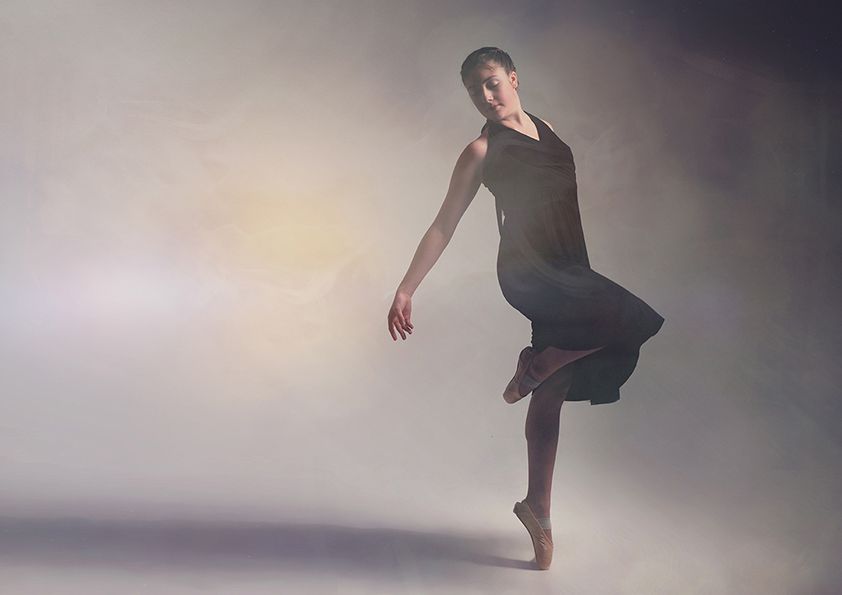 Contemporary dancer in black dress creates flowing movement against misty background.