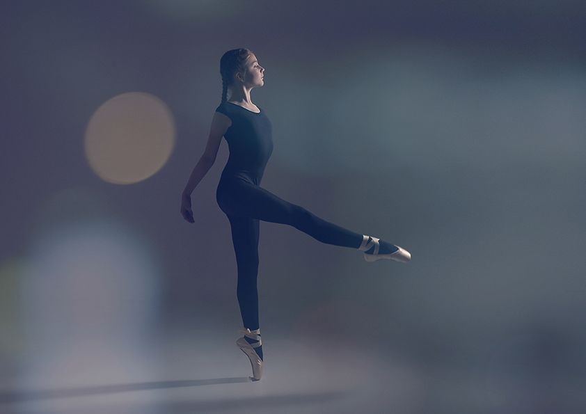 Ballet dancer executes perfect arabesque pose against soft focus background.