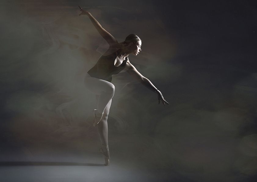 Atmospheric dance photo with dramatic lighting shows ballet pose in misty setting.