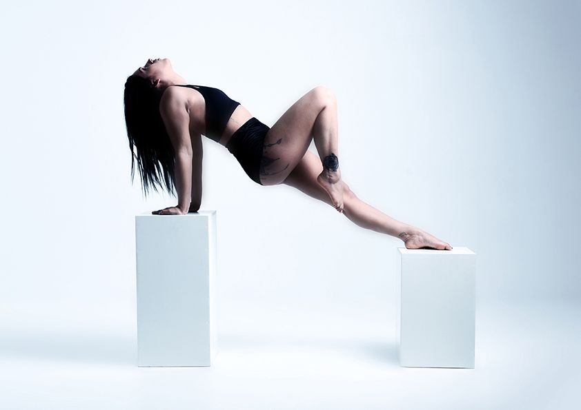 Dancer in black attire creates geometric pose between white blocks in studio setting.