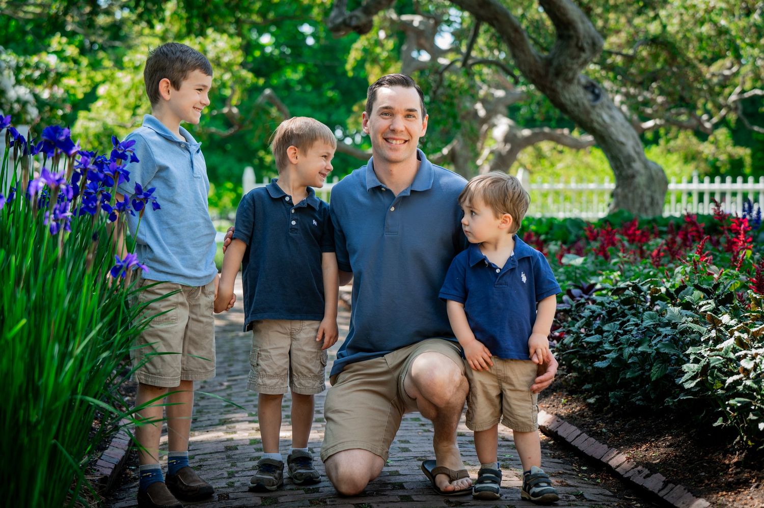 A family group poses together on a garden path surrounded by purple iris flowers and lush greenery.