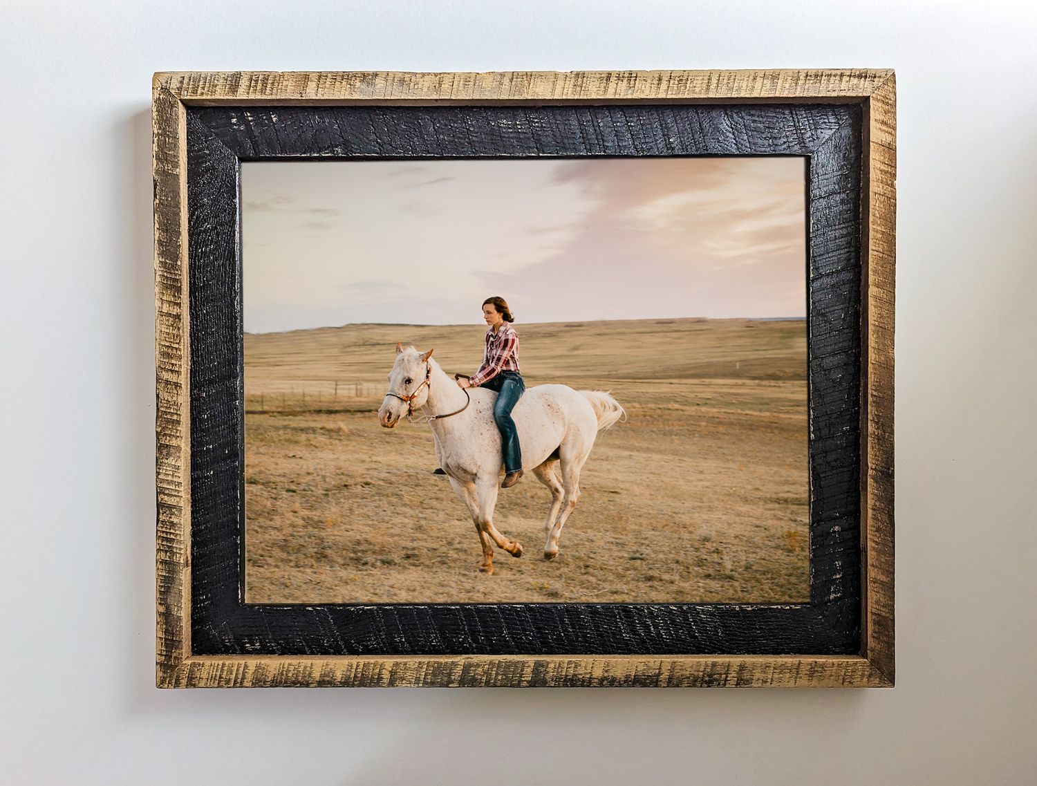 Framed photograph of someone riding a white horse across golden grasslands at sunset.