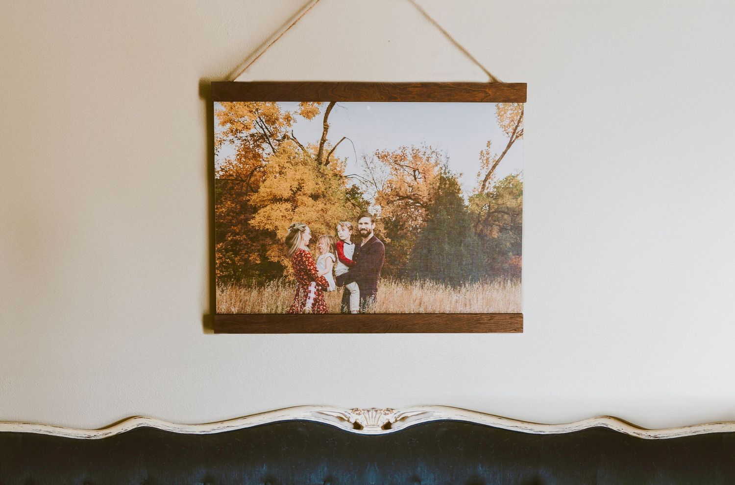 A vintage wall-mounted photograph showing silhouettes of people in an autumn landscape hanging above a white cabinet.