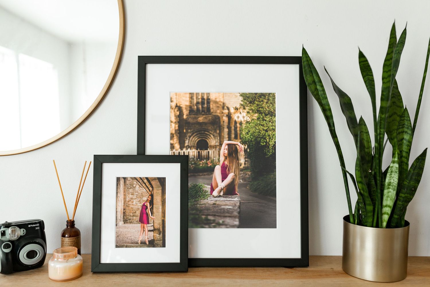 Modern home decor display with black frames, gold mirror, vintage camera, and snake plant in metallic planter.