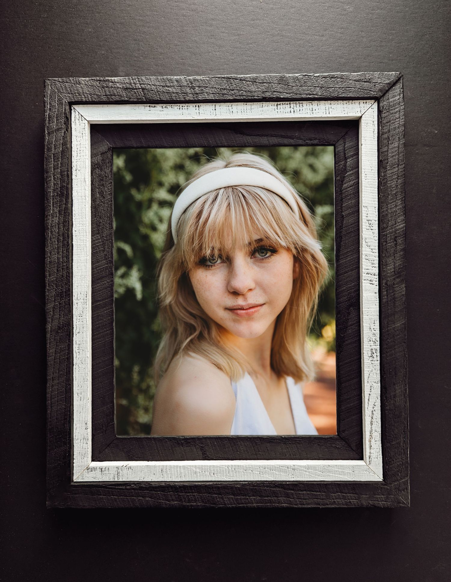 A framed portrait photograph in a rustic white and dark wooden frame mounted on a gray wall.