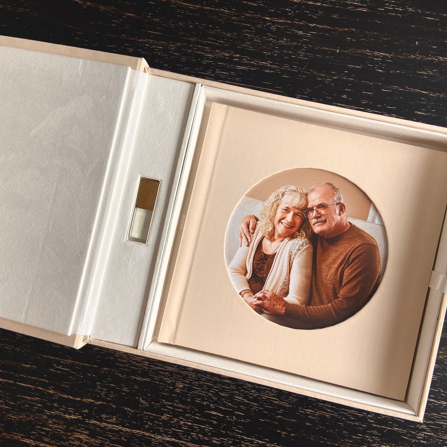 A circular portrait photo mounted in an elegant white presentation box with USB drive on dark wooden surface.