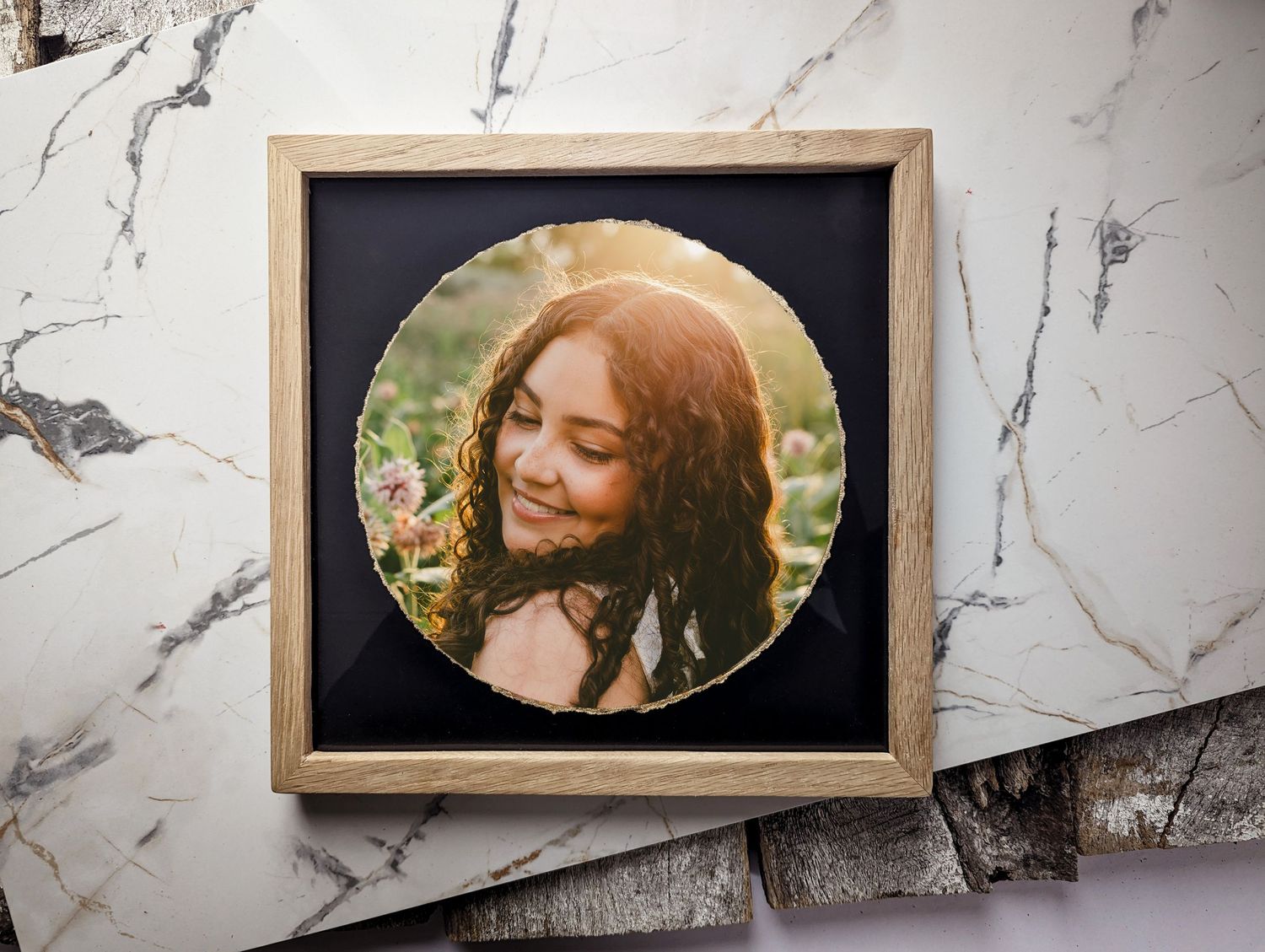 A circular photo portrait displayed in a wooden frame against a marble background.
