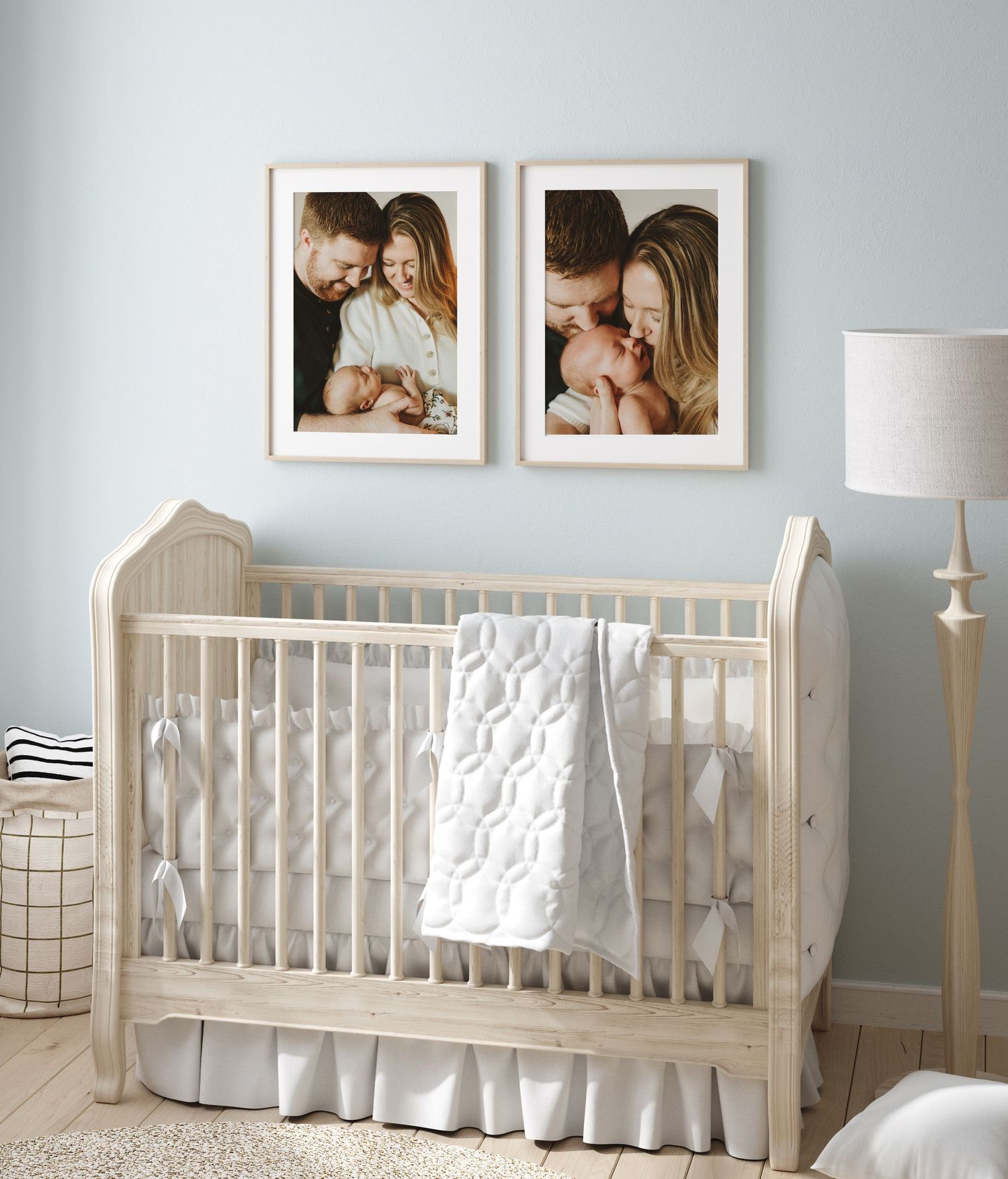 A white nursery with a classic wooden crib, framed family photos above, and a fabric lamp against pale blue walls.