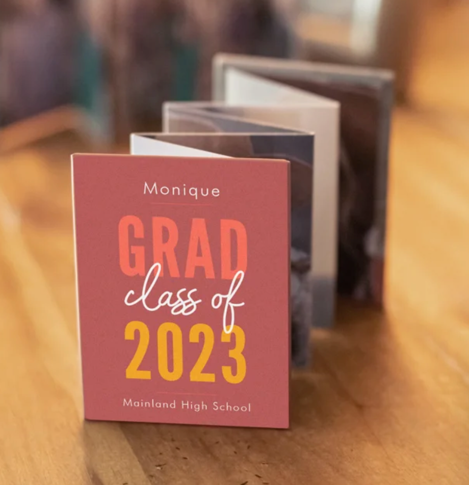 A graduation announcement card for Monique from Mainland High School Class of 2023 rests on a wooden surface.