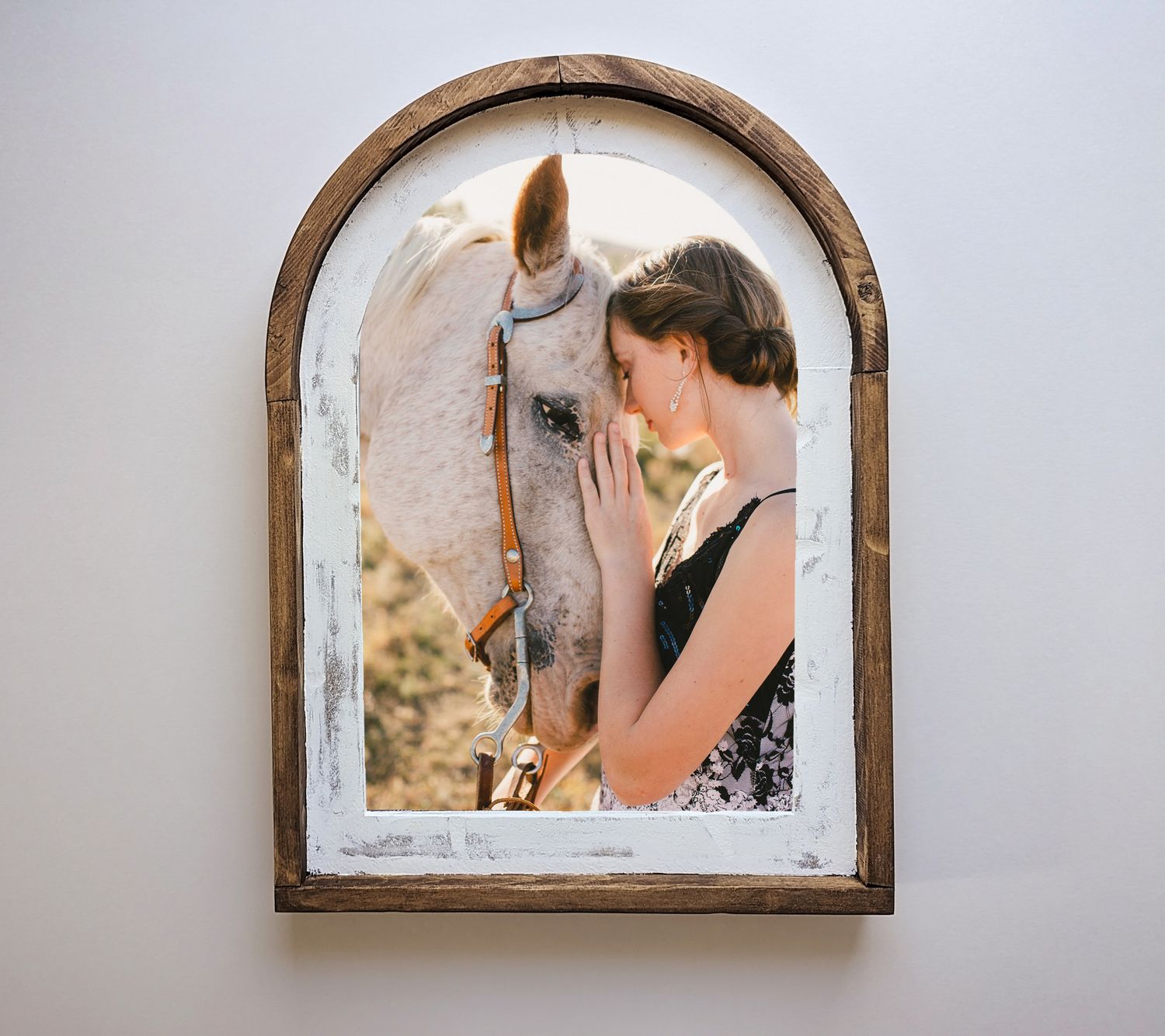 A white horse and a companion share a tender moment through a rustic arched window frame.