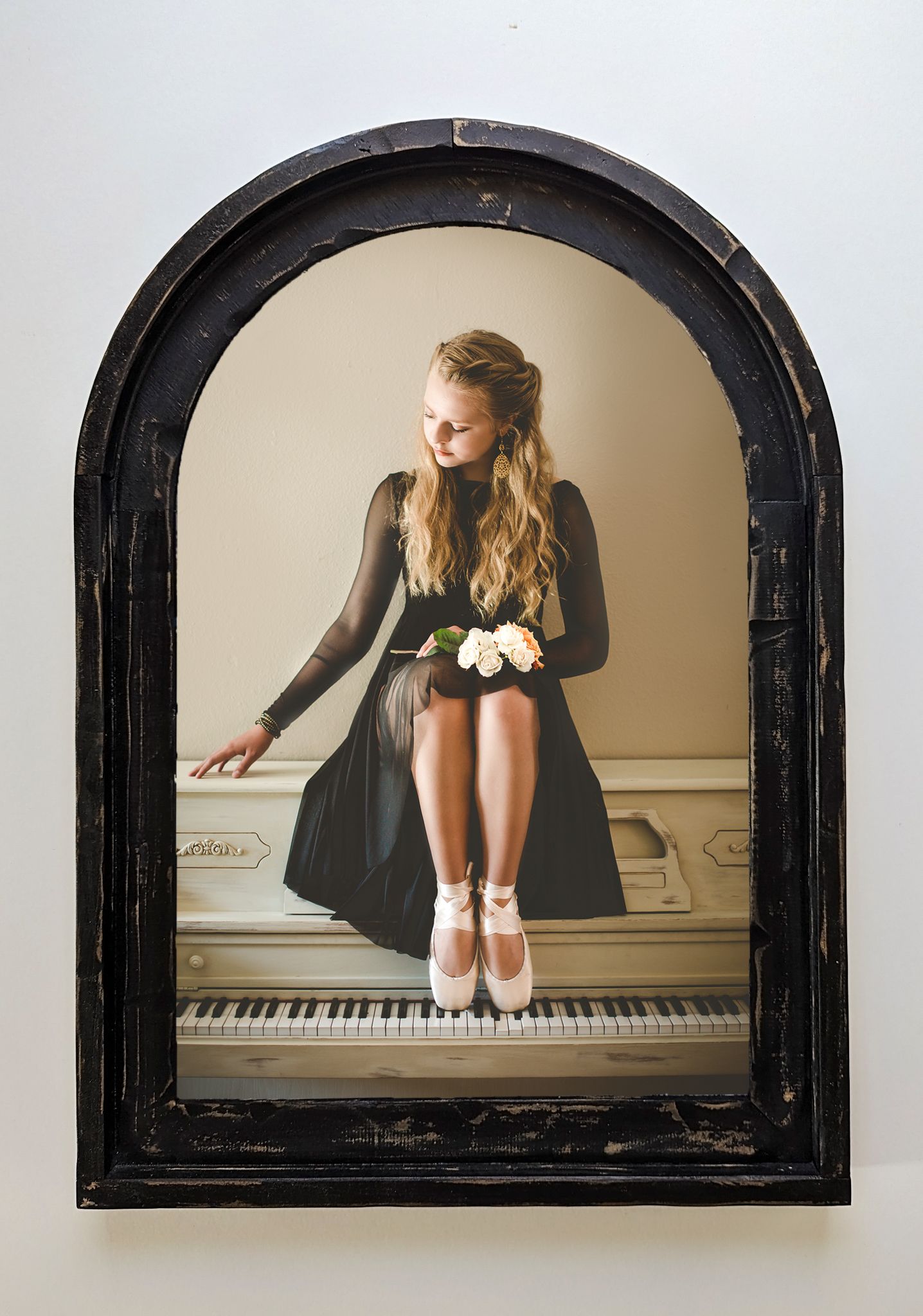 Ballet dancer in black dress sits gracefully on piano keys with white flowers in artistic arched frame composition.