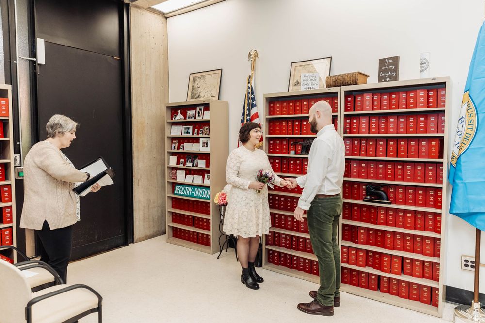 Three people browse books on red shelves in a library or archive room.
