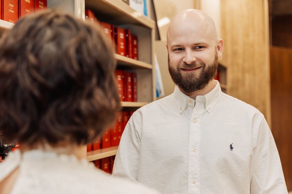 Two people having a conversation in front of red bookshelves.
