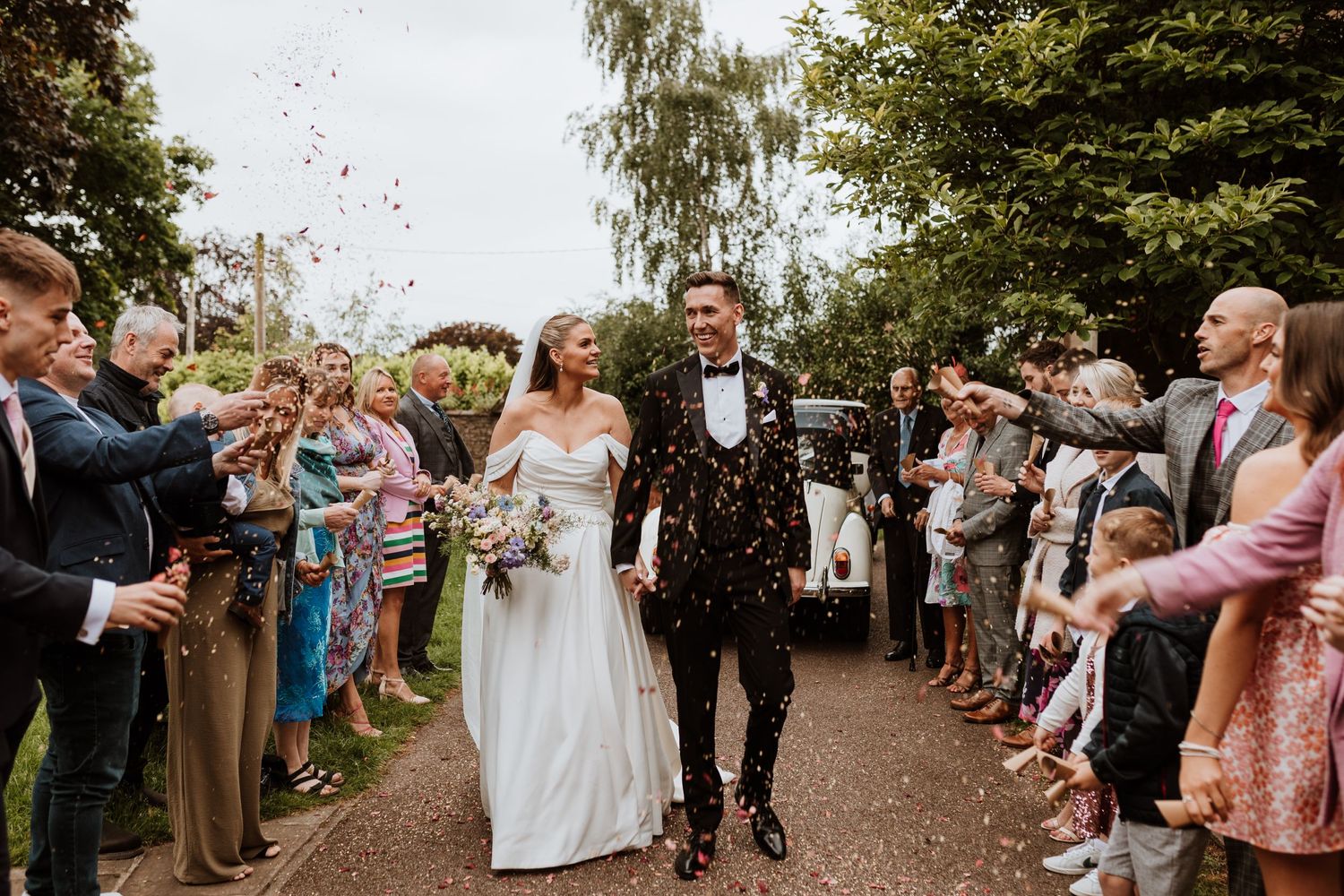 Guests shower couple with confetti along garden path during joyful wedding celebration.