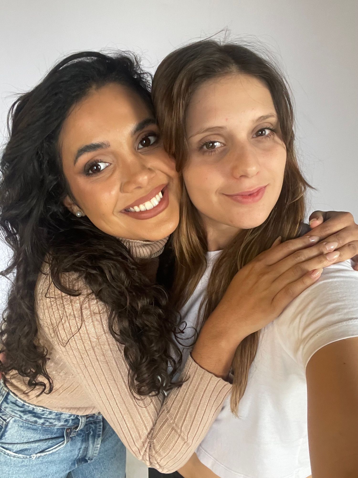 Close-up selfie of two friends embracing and smiling warmly at the camera.