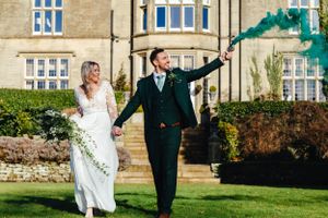 Newlyweds celebrate with smoke bombs while walking through manicured garden grounds.