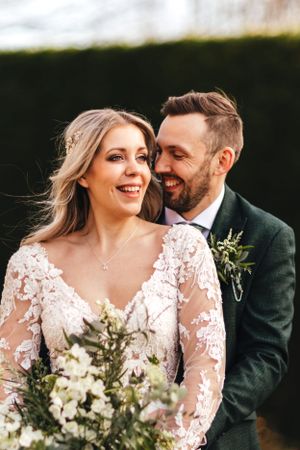Candid wedding portrait capturing joyful laughter against garden hedge backdrop.