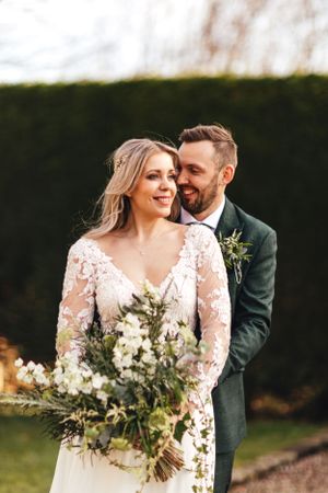 Intimate wedding portrait showing tender moment with lush greenery bouquet against garden background.