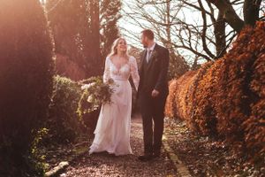 Sunlit wedding portrait on garden path with golden afternoon light filtering through trees.