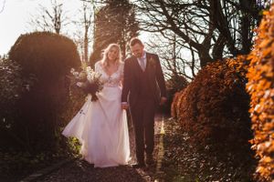 Couple walks hand in hand through a garden path during golden hour on their wedding day.