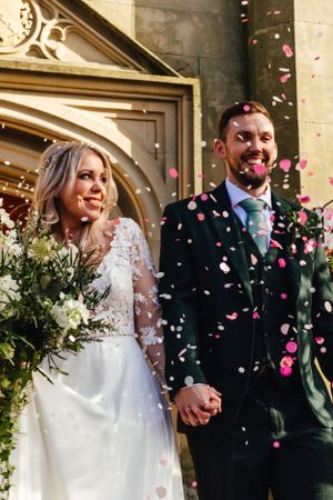 Newlyweds celebrate outside a church entrance as pink confetti falls around them on their wedding day.
