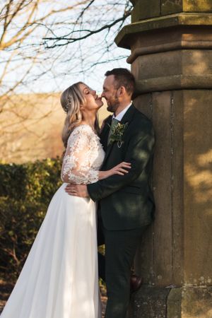 Romantic wedding moment captured against a stone pillar with countryside views in the background.