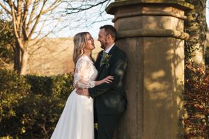 Intimate wedding portrait by a stone pillar with scenic countryside views and winter trees.