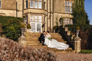 A wedding couple poses on grand stone steps of a historic mansion.